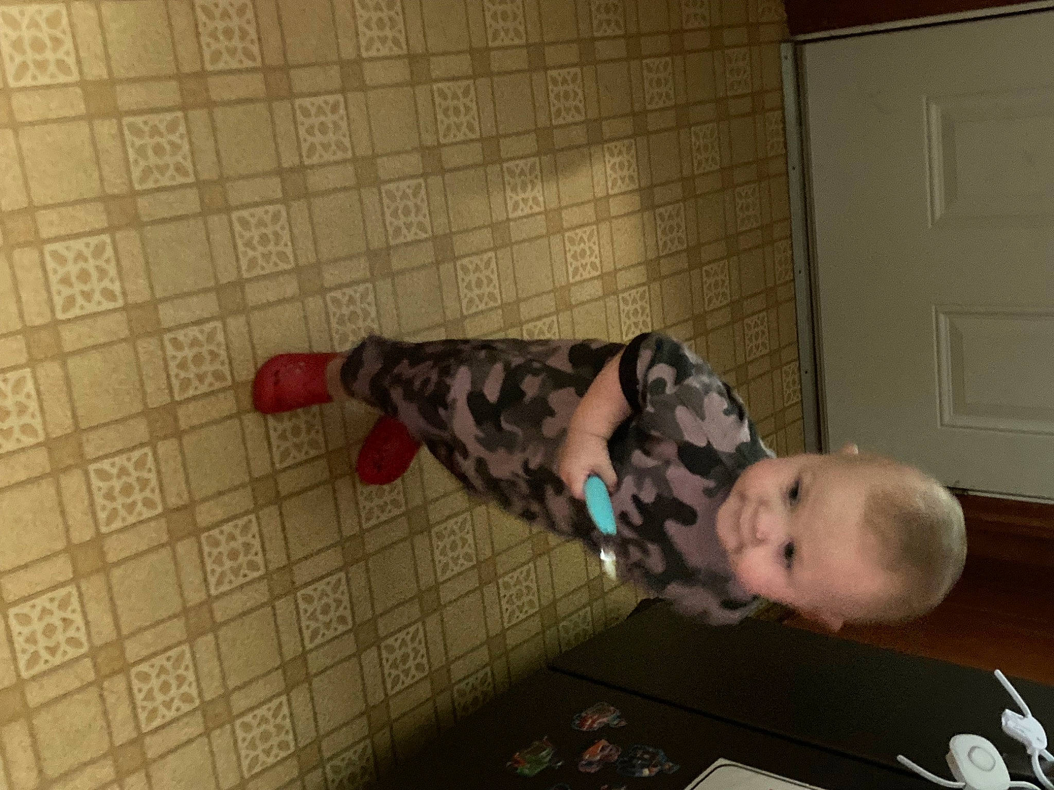 Jax is registered to the contest to win money with this photo: baby, baby_toddler_clothing, child, comfort, door, elbow, floor, flooring, fun, hardwood, human_body, light_switch, military_camouflage, pattern, person, room, sitting, toddler, wood