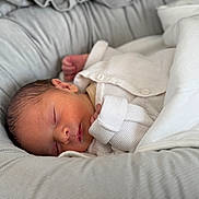 Adam participe au concours pour gagner de l'argent avec cette photo : newborn, baby, sleeping, white_clothing, knitwear, blanket, cushion, cozy, peaceful, infant, soft_texture, resting, indoors, portrait, head, face, hand, closeup, comfort, nest