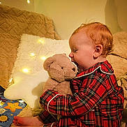 Harper is registered to the contest to win money with this photo: baby, teddy_bear, plaid_pajamas, red_clothing, cozy, blanket, star_pillow, fairy_lights, soft_toy, child, indoor, bedtime, cute, smiling, comfort, warm_lighting, couch, playful, portrait, infant