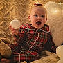 Harper is registered to the contest to win money with this photo: baby, child, pajamas, plaid, red_clothing, blanket, pillow, fairy_lights, soft_texture, smiling, happy, indoors, cute, toy, cozy, warm_lighting, face, person, sitting, holiday