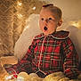Harper is registered to the contest to win money with this photo: baby, child, pajamas, plaid, blanket, pillow, soft_toy, fairy_lights, cozy, indoor, cute, surprised, expression, warm_lighting, bedroom, holiday, decor, infant, portrait, comfortable