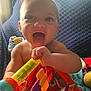 baby, child, tongue_out, toy, colorful, indoor, blue_blanket, happy, smiling, infant, playtime, hand, face, window_light, soft_light, numbers, plastic_toy, closeup, cute, cheerful