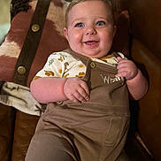 Joey joined the competition — help win amazing prizes! baby, child, smiling, blue_eyes, overalls, shirt, patterned_clothing, blanket, horse_pattern, leather_chair, indoor, portrait, happy, cute, infant, closeup, sitting, cozy, plush, warm_lighting