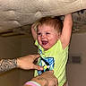toddler, child, smiling, happy, laughing, indoor, tattoo, hand, lifting, green_shirt, cushion, playful, person, baby, light_skin, short_hair, fun, joy, diaper, holding
