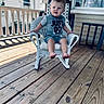 baby, barefoot, child, curious, daylight, expression, face, grey_clothing, outdoor, person, porch, railing, rocking_chair, shirt, shorts, sitting, toddler, wicker_chair, window, wooden_floor