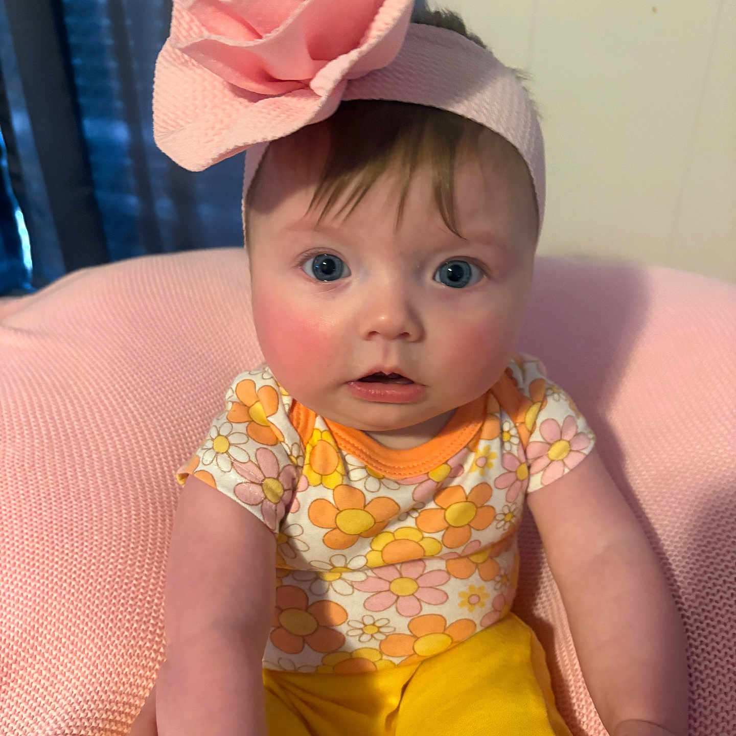 Sadie joined the competition — help win amazing prizes! baby, child, infant, pink_headband, flower, floral_clothing, yellow_pants, cushion, soft_texture, indoor, portrait, blue_eyes, curious_expression, hand_support, seated, closeup, cute, skin, person, headwear