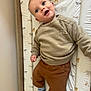 baby, child, infant, smiling, blue_eyes, beige_sweater, brown_pants, patterned_socks, changing_pad, animal_print, wooden_frame, indoor, cute, happy, portrait, person, clothing, wall, laying_down, baby_bed