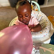 Royalty is registered to the contest to win money with this photo: baby, balloon, child, cushion, hair, infant, indoor, person, pink, seat, toy, young_child, curious, baby_seat, carpet, home, playing, skin, clothing, closeup