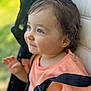 toddler, child, smiling, face, blue_eyes, curly_hair, stroller, seatbelt, orange_clothing, blurred_background, outdoor, closeup, portrait, happy, baby, person, natural_light, expression, sitting, cute