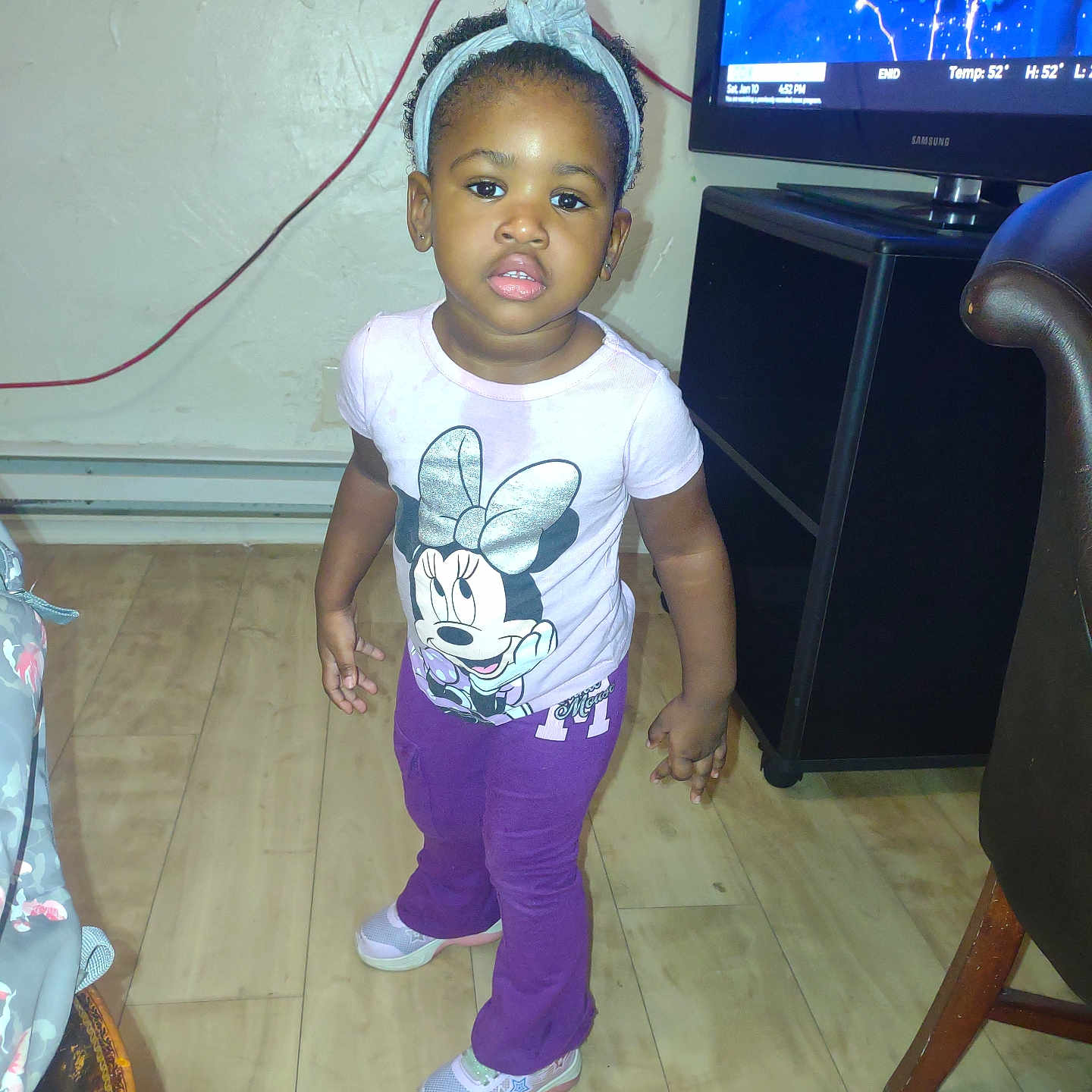 Danolia is registered to the contest to win money with this photo: casual_clothing, child, curly_hair, earrings, expression, furniture, headband, home, indoor, living_room, minnie_mouse, person, purple_pants, sneakers, standing, television, toddler, tshirt, weather_forecast, wood_floor