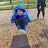 baby, child, swing, playground, blue_jacket, smile, outdoor, woman, park, grass, trees, wood_chips, happy, person, casual_clothing, daytime, fun, play, jacket, footwear