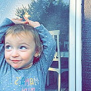 Saylor is registered to the contest to win money with this photo: toddler, child, polka_dot, gray_shirt, smiling, hands_up, glass_door, wicker_chair, outdoor, reflection, window_screen, playful, curly_hair, person, portrait, happy, daylight, wall, texture, casual_clothing