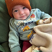 Elijah joined the competition — help win amazing prizes! baby, child, beanie, hat, sweater, blanket, fleece, green, orange, cute, portrait, infant, cozy, warm, smile, hand, face, clothing, indoors, comfort