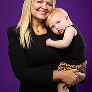 Willow joined the competition — help win amazing prizes! woman, child, portrait, studio, purple_background, black_clothing, smile, blonde_hair, baby, leopard_print, holding, cute, happy, fashion, person, studio_lighting, mother_and_child, toddler, affection, footwear