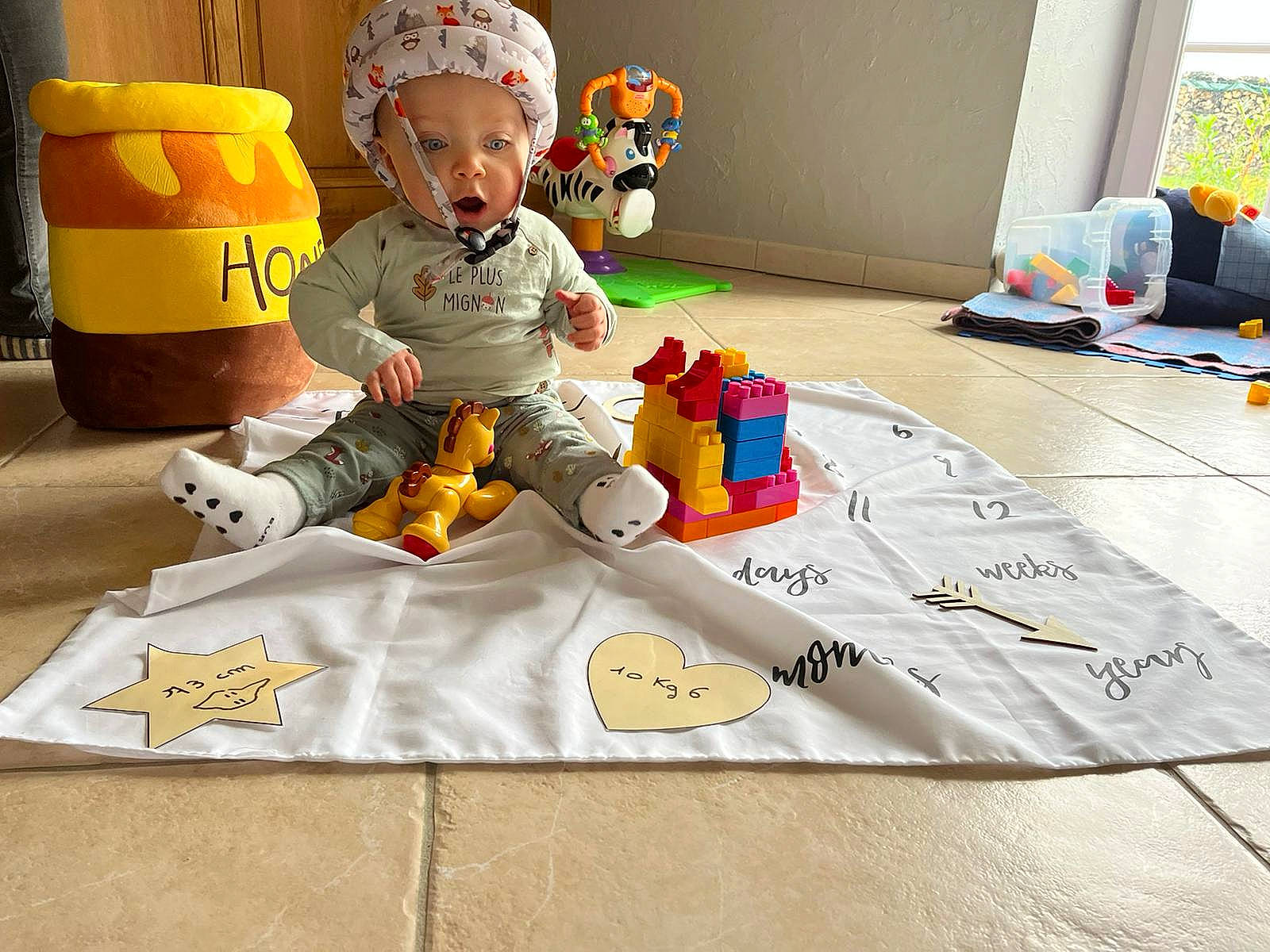 Mahe a rejoint le concours — aidez-le/la à gagner de superbes lots ! art, baby, baby_toddler_clothing, baby_toys, carmine, child, flooring, font, fun, handwriting, headwear, linens, person, play, room, sitting, stuffed_toy, toddler, toy, visual_arts