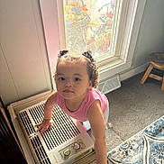 Maddilynn is registered to the contest to win money with this photo: toddler, child, indoor, curly_hair, pink_shirt, window, air_conditioner, carpet, stool, home, light, hands, curiosity, person, portrait, standing, floor, furniture, hair_ties, expression