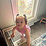toddler, child, indoor, curly_hair, pink_shirt, window, air_conditioner, carpet, stool, home, light, hands, curiosity, person, portrait, standing, floor, furniture, hair_ties, expression