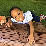 Adrian is registered to the contest to win money with this photo: child, smiling, cushion, toy, green_turf, indoor, playtime, happy, casual_clothing, shorts, sneakers, hand, face, person, playground, fun, relaxing, wood_pattern, reaching, friend