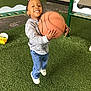 Adrian is registered to the contest to win money with this photo: child, smiling, basketball, playground, artificial_turf, jeans, sneakers, long_sleeve_shirt, outdoor, playing, happy, person, toy, sports, active, young, fun, recreation, boy, casual