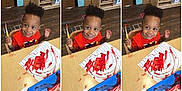 Adrian is registered to the contest to win money with this photo: child, toddler, smiling, painting, red_paint, brush, artwork, table, classroom, wooden_floor, chair, orange_shirt, messy, creative, happy, indoor, person, expression, young, fun