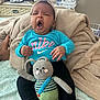baby, yawning, headband, blue_shirt, nike_logo, black_pants, crocheted_toy, bunny_toy, blanket, folded_towels, bedspread, television, news, hand, foot, indoor, person, child, soft_texture, home