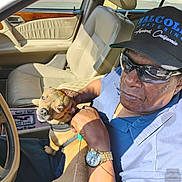 Pj Beckum is registered to the contest to win money with this photo: animal, cap, car_interior, casual, clothing, dashboard, dog, hand, leather, man, pet, portrait, resting, seat, seatbelt, sunglasses, sunlight, vehicle, watch, window