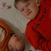 Azelya a rejoint le concours — aidez-le/la à gagner de superbes lots ! child, baby, infant, face, person, lying_down, orange_clothing, ornaments, christmas_decor, holiday, cute, indoor, soft_surface, curly_hair, sibling, playful, expression, head_scratching, blanket, festive