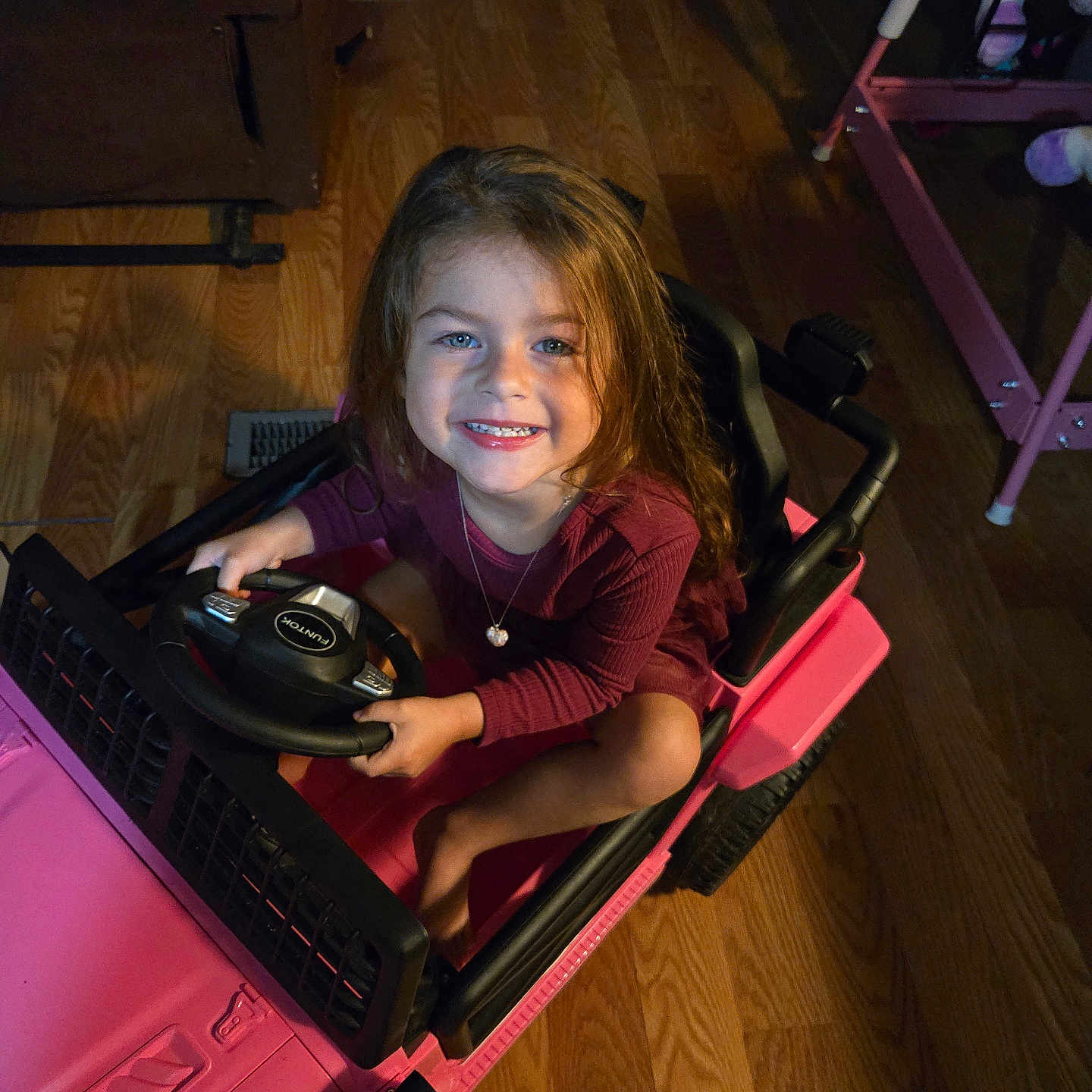 Ellie joined the competition — help win amazing prizes! child, girl, smiling, blue_eyes, toy_car, pink, indoor, wooden_floor, steering_wheel, happy, long_hair, necklace, clothing, person, play, small_vehicle, floor, seat, hands, portrait