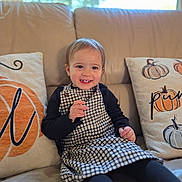 Vana joined the competition — help win amazing prizes! toddler, child, smiling, sitting, couch, pillows, pumpkin, window, indoor, clothing, dress, black_sleeves, happy, face, hair, home, cozy, natural_light, cute, portrait