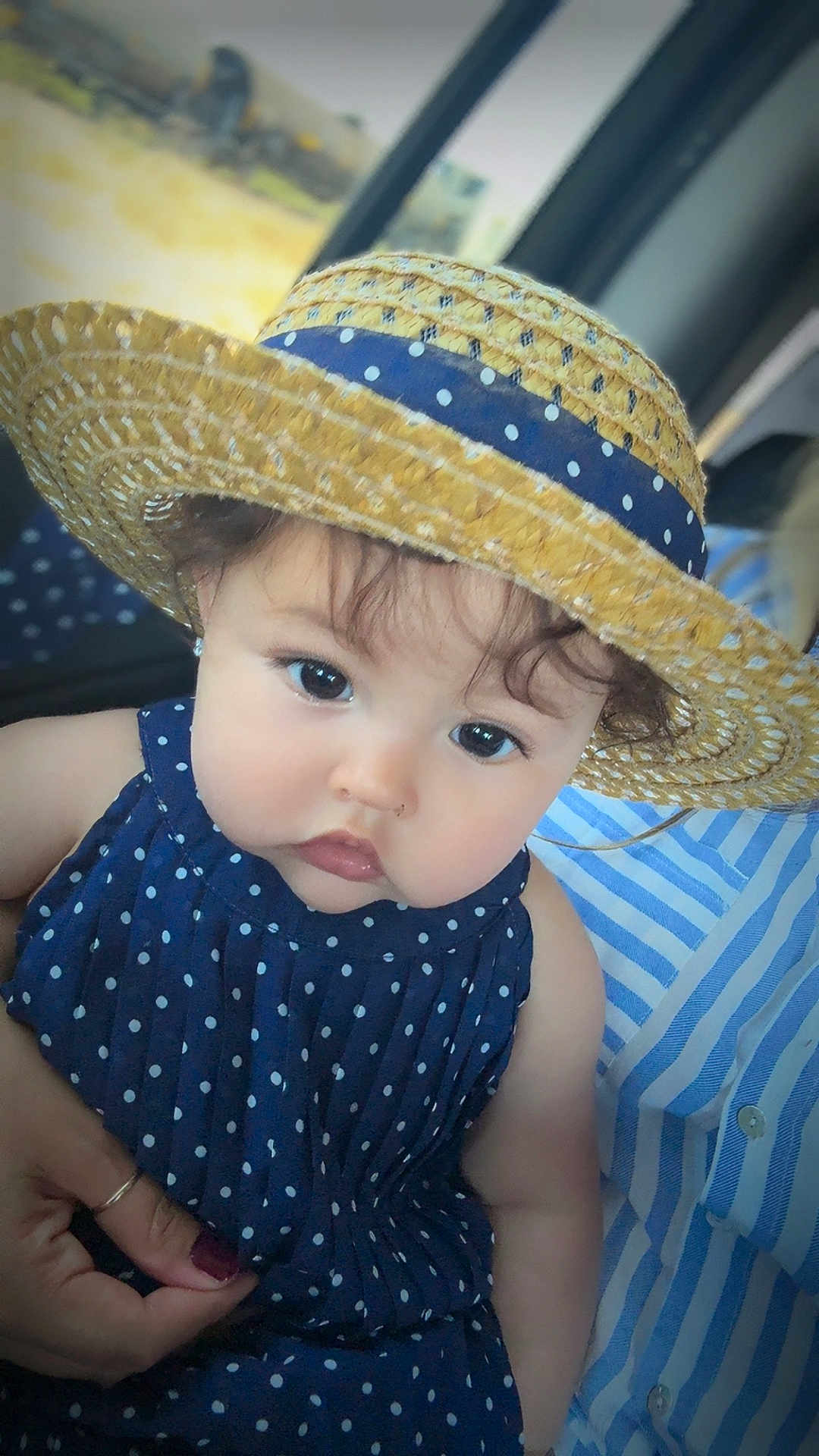 Arlette is registered to the contest to win money with this photo: baby, child, hat, straw_hat, polka_dot, dress, navy_blue, face, eyes, curly_hair, hand, striped_shirt, adult, person, portrait, close_up, indoors, cute, holding, fashion