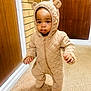 Jesse is registered to the contest to win money with this photo: toddler, child, onesie, bear_ears, quilted_clothing, indoor, carpet, walking, baby, person, hallway, door, brick_wall, footwear, cute, young_child, standing, apparel, head_covered, childhood