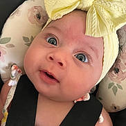 Omi is registered to the contest to win money with this photo: baby, headband, yellow_bow, car_seat, floral_pattern, straps, face, eyes, infant, cute, child, closeup, expression, skin, person, seatbelt, adorable, young, portrait, clothing