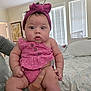 Omi is registered to the contest to win money with this photo: baby, infant, pink_outfit, headband, hands, bedroom, bed, window_blinds, person, cute, chubby_cheeks, holding, indoor, soft_light, portrait, clothing, skin, face, expression, young_child