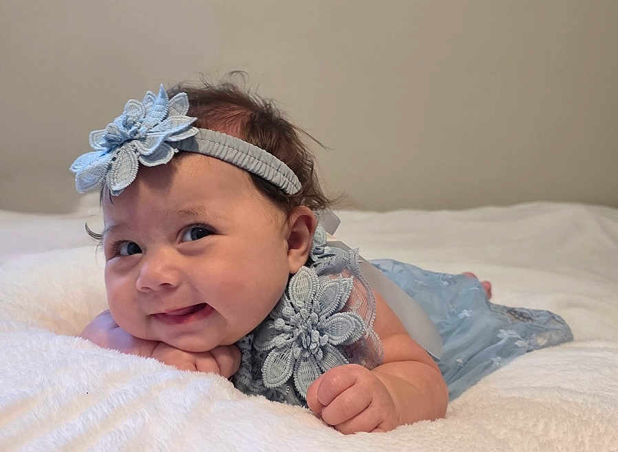 Omi joined the competition — help win amazing prizes! baby, infant, blue_dress, headband, smile, lying_down, blanket, cute, face, hand, cheeks, skin, person, young_child, portrait, indoor, soft_texture, expression, happy, baby_clothing