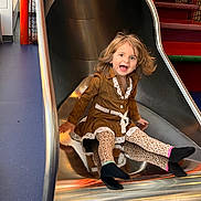 Annalea joined the competition — help win amazing prizes! child, toddler, girl, smiling, happy, indoor, playground, slide, sitting, portrait, face, hair, dress, brown_clothing, lace, patterned_tights, socks, play_area, colorful, playful