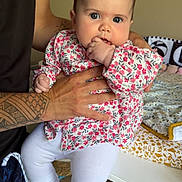 Valentina participe au concours pour gagner de l'argent avec cette photo : baby, child, tattoo, hand, floral_clothing, white_leggings, sneakers, indoor, changing_table, baby_supplies, person, cute, infant, blue_eyes, holding, fingers_in_mouth, home, casual, patterned_clothing, decor