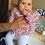 baby, child, tattoo, hand, floral_clothing, white_leggings, sneakers, indoor, changing_table, baby_supplies, person, cute, infant, blue_eyes, holding, fingers_in_mouth, home, casual, patterned_clothing, decor