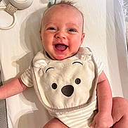 Connor is registered to the contest to win money with this photo: baby, smiling, infant, bib, cute, happy, lying_down, striped_clothing, face, head, skin, human, child, newborn, indoor, closeup, expression, baby_bib, toy, pacifier