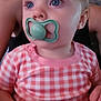 Halle is registered to the contest to win money with this photo: baby, pacifier, blue_eyes, pink_clothing, checkered_pattern, child, infant, person, portrait, cute, sitting, hand, indoor, soft_light, young_child, face, skin, head, adult_background, calm