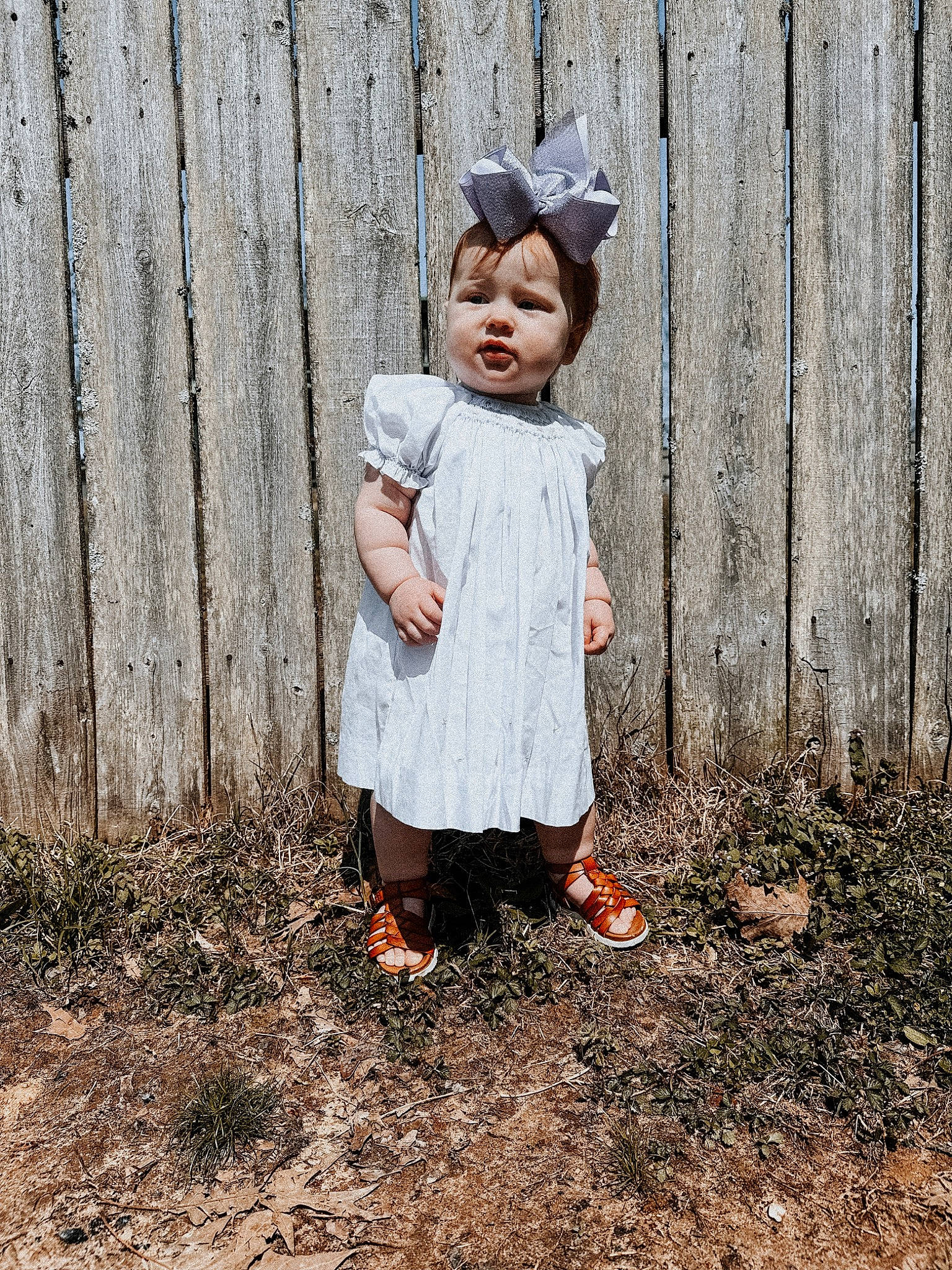 Payton is registered to the contest to win money with this photo: baby_toddler_clothing, child, dress, fence, fun, grass, happy, landscape, pattern, people_in_nature, person, portrait_photography, sandal, sitting, sleeve, soil, toddler, tree, vintage_clothing, wood
