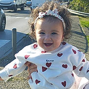 Aryam a rejoint le concours — aidez-le/la à gagner de superbes lots ! toddler, child, curly_hair, headband, heart_pattern, white_clothing, outdoor, sunlight, smile, happy, person, holding_hands, road, vehicles, trees, sidewalk, daytime, casual_wear, cute, playful