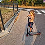 child, scooter, outdoor, sunlight, shadow, fence, trees, road, shorts, shoes, bare_chest, sidewalk, play, summer, casual, nature, happy, boy, recreation, daytime