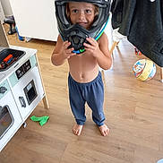 Lyham participe au concours pour gagner de l'argent avec cette photo : child, helmet, barefoot, blue_pants, toy, wooden_floor, indoor, play, smiling, furniture, ball, shirtless, happy, person, home, floor, cabinet, chair, helmet_held, curiosity