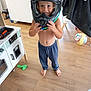 child, helmet, barefoot, blue_pants, toy, wooden_floor, indoor, play, smiling, furniture, ball, shirtless, happy, person, home, floor, cabinet, chair, helmet_held, curiosity