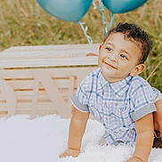 Josiah is registered to the contest to win money with this photo: toddler, child, smiling, curly_hair, blue_shirt, sandals, blanket, balloons, wooden_letters, one, outdoor, grass, birthday, celebration, happy, cute, portrait, crawling, baby, sunny