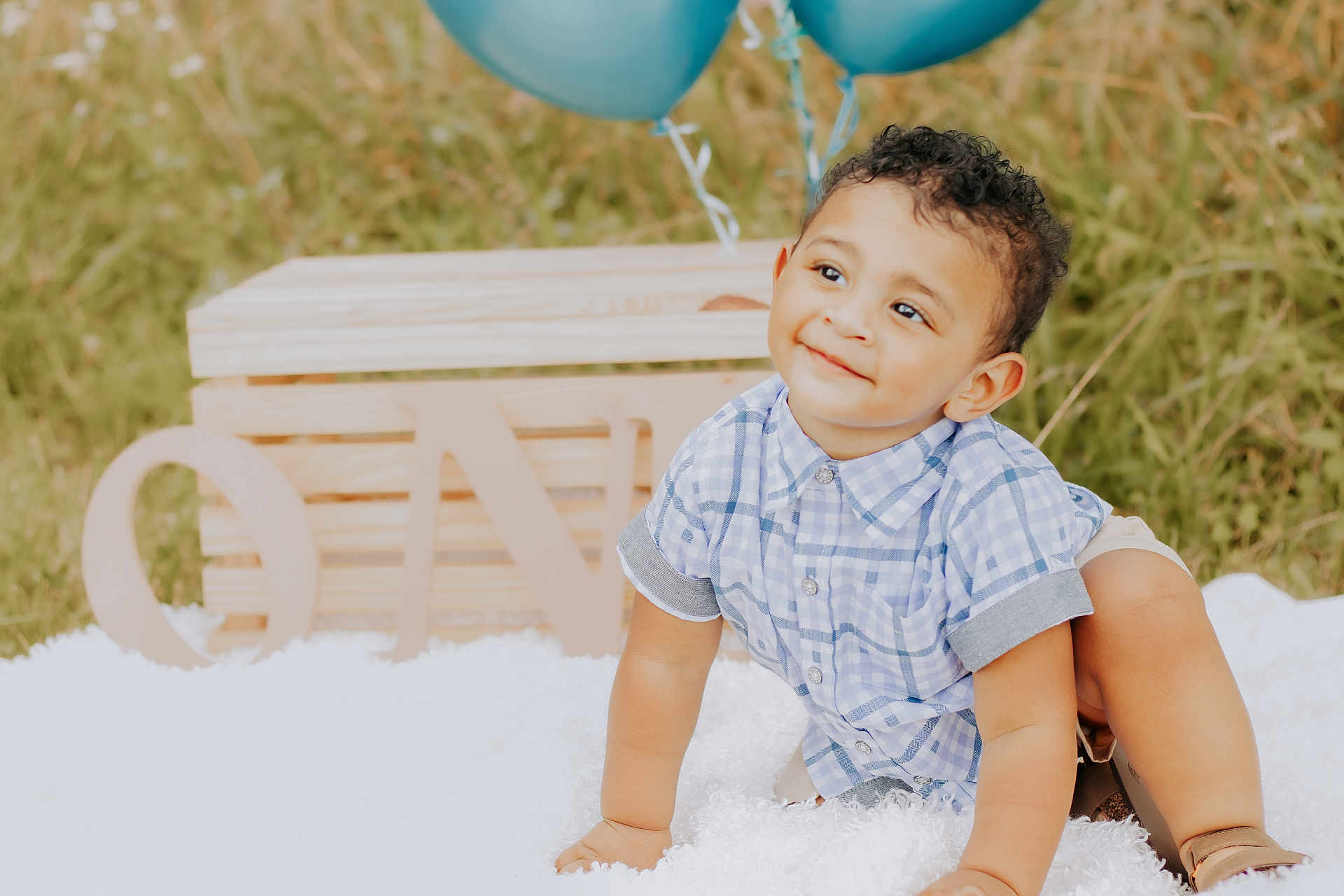 Josiah is registered to the contest to win money with this photo: toddler, child, smiling, curly_hair, blue_shirt, sandals, blanket, balloons, wooden_letters, one, outdoor, grass, birthday, celebration, happy, cute, portrait, crawling, baby, sunny