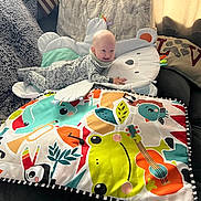 Makai joined the competition — help win amazing prizes! baby, child, play_mat, pillow, bear_pillow, blanket, couch, smile, indoors, curtains, colorful, cozy, head, face, person, furniture, toy, pattern, soft, happy