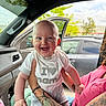 Makai is registered to the contest to win money with this photo: baby, child, smiling, tattoo, shirt, clothing, car_interior, car_door, window, person, holding, happy, face, blue_eyes, short_sleeves, jeans, outdoor, tree, vehicle, seat