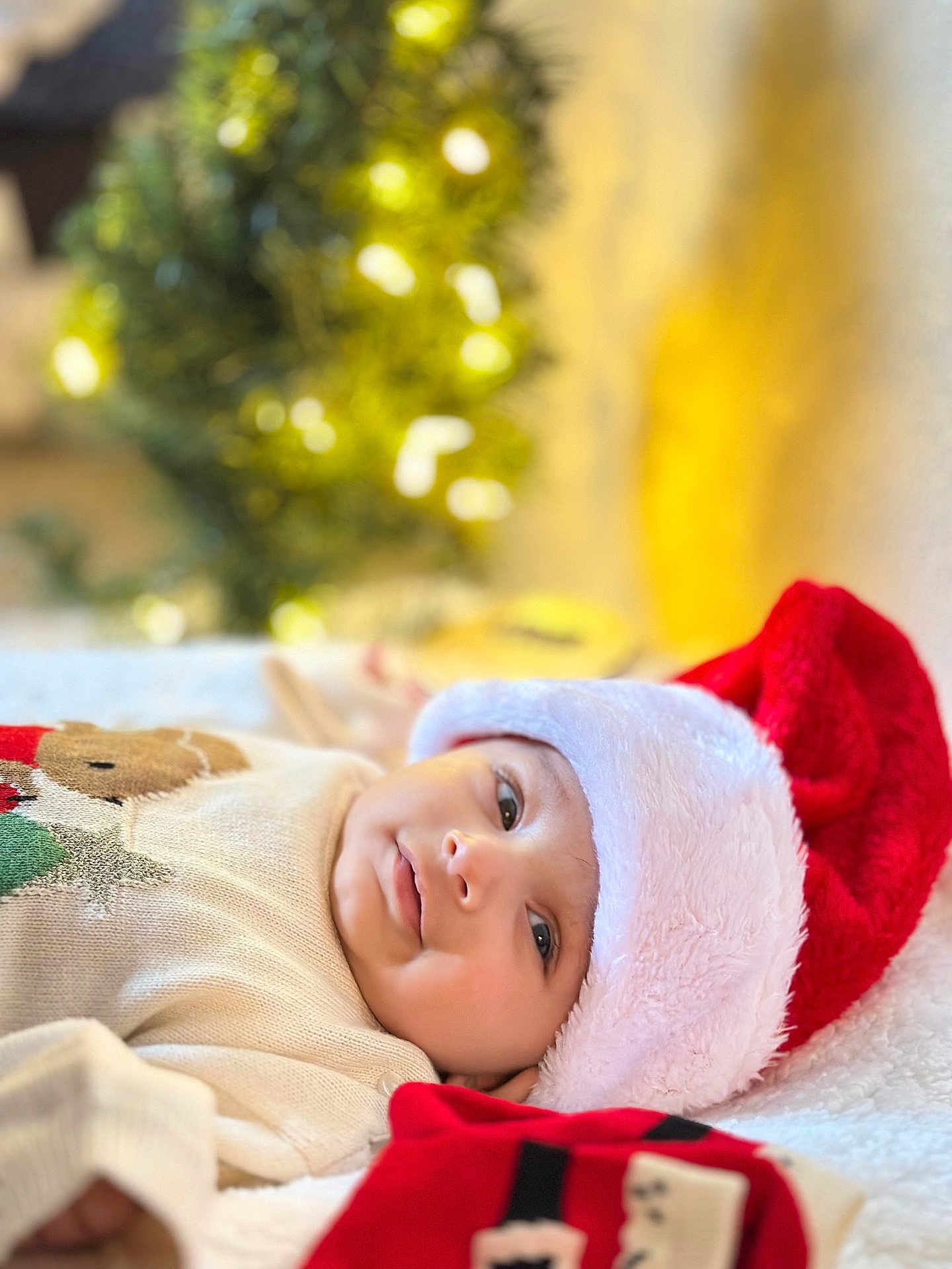 Agastya joined the competition — help win amazing prizes! baby, santa_hat, christmas, holiday, infant, smile, cozy, sweater, soft_blanket, festive, warm_lighting, indoors, portrait, cute, lying_down, holiday_decor, blurred_background, child, celebration, happy