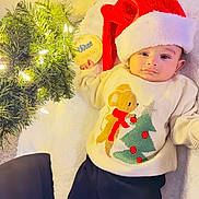 Agastya is registered to the contest to win money with this photo: baby, infant, santa_hat, sweater, christmas_tree, holiday, festive, lights, blanket, wooden_sign, three_months, cute, smiling, indoors, decorations, cozy, lying_down, child, winter, celebration
